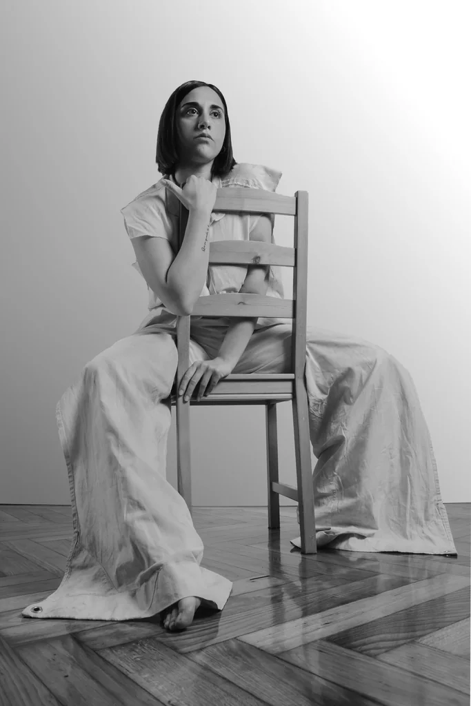 Seated backwards on a wooden chair in white linen