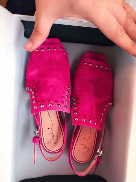 Pink studded suede sandals in their shoebox, a hand lifting them out