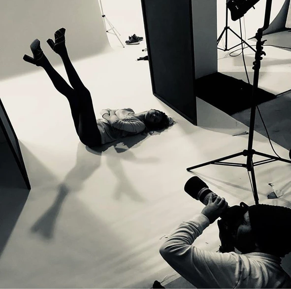Behind the scenes: a model with legs raised against the white studio wall, the photographer shooting from the floor