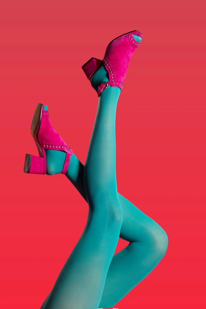 A leg in teal tights kicked up, pink studded heel against a red backdrop