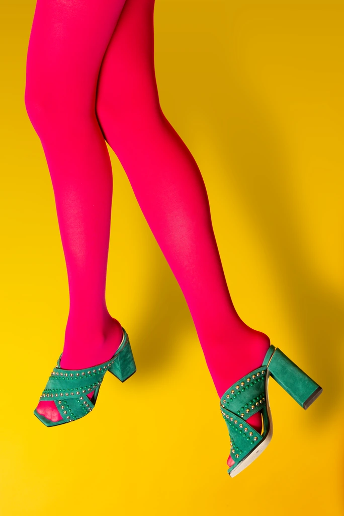 Pink tights and teal studded heels crossing on a yellow backdrop