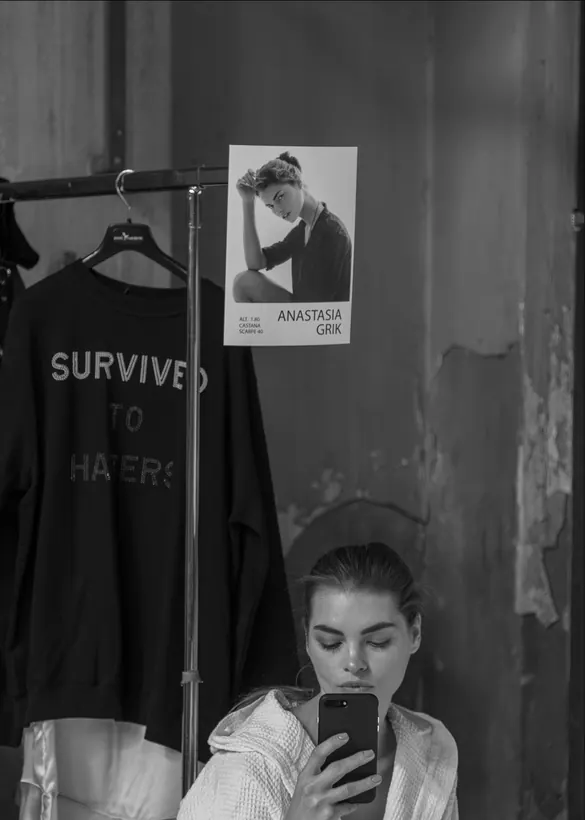 A casting card pinned above a rail, a model checking her phone below