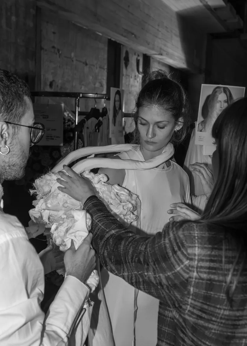 Dressers fitting a pale ruffled garment on a model