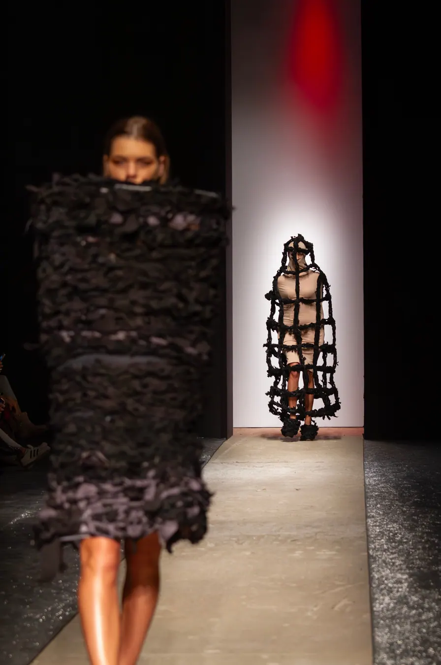 Two models in black open-weave cage garments on the runway